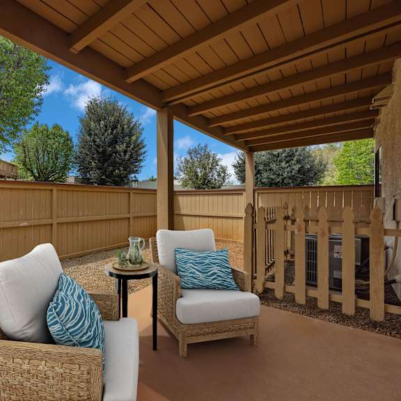 a patio with a wicker chair and a small table with a green cup on it.