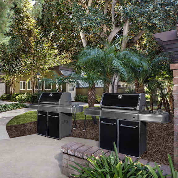 two grills in a barbeque area located in a landscaped yard.