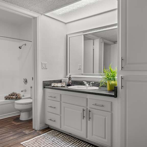 a split bathroom with a large mirror and white cabinets with black countertop.
