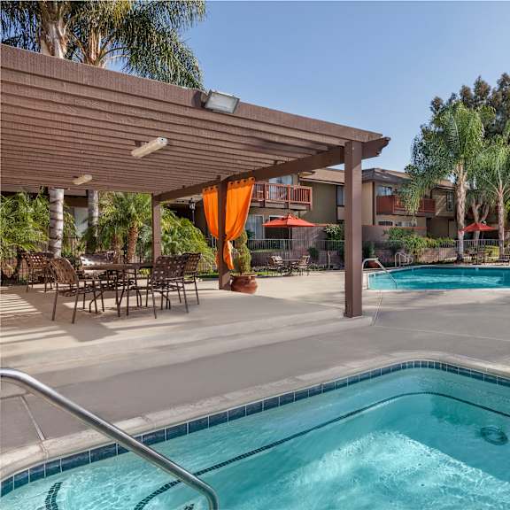 a pool and jacuzzi with a patio with chairs and a table.