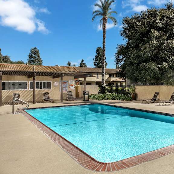 a large swimming pool surrounded by a concrete patio and lounge chairs.