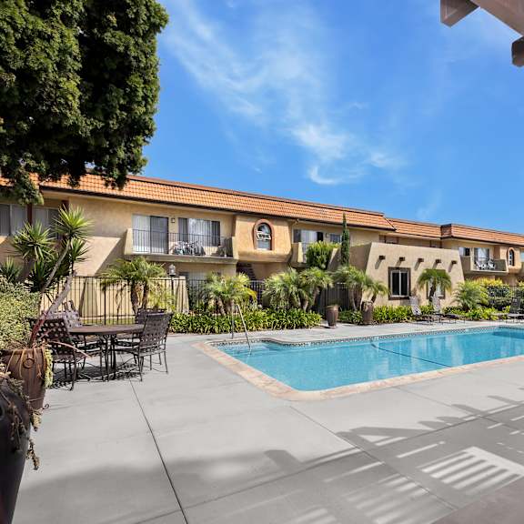 a pool area with a table and chairs and a building in the background.