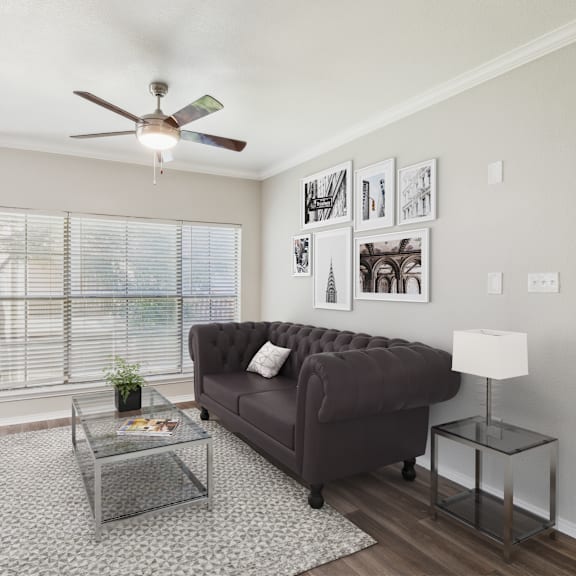 a living room with a grey couch, a glass coffee table, and a ceiling fan.