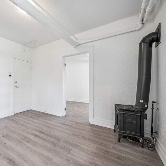 a wood burning stove sits in a corner of a white room with wood floors and white walls.
