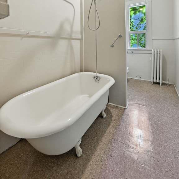 a white bathtub with a shower head and a window in the bathroom.
