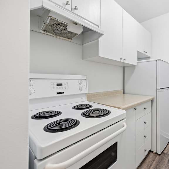 a white stove with four burners is in a kitchen with white cabinets.