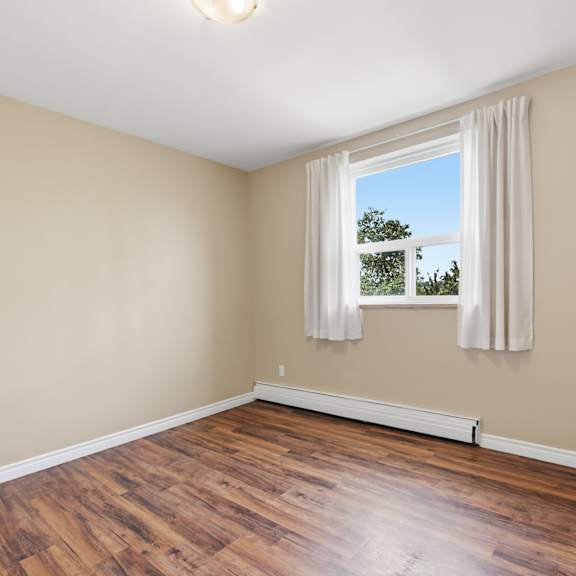 a room with wooden floors and a window with white curtains.
