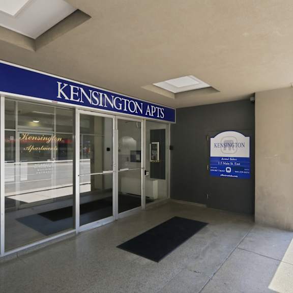 the image shows the entrance to kensington apartments with a blue signboard and a glass door.