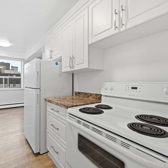 a white kitchen with a stove, refrigerator, and cabinets.