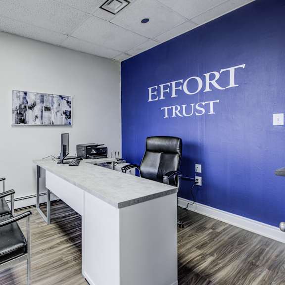 a room with a white desk and a black chair with a blue wall that says effort trust.