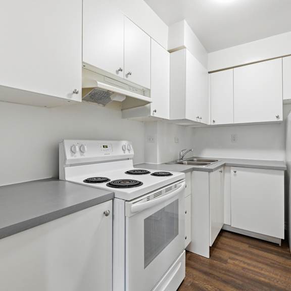 a white kitchen with a stove, sink, and refrigerator.