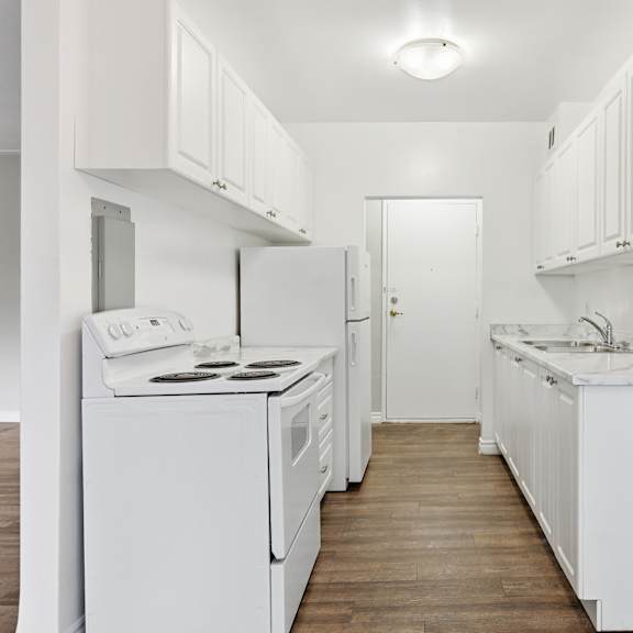 a white kitchen with a white fridge, stove, and sink.