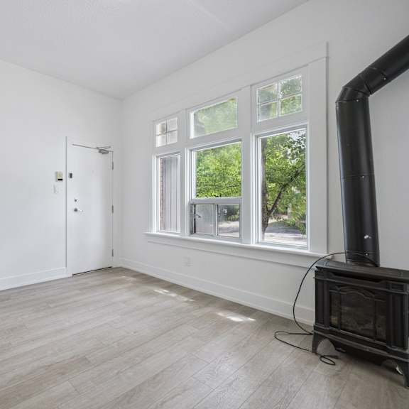 a room with a wood floor, a wood stove, and a window with a view of trees.