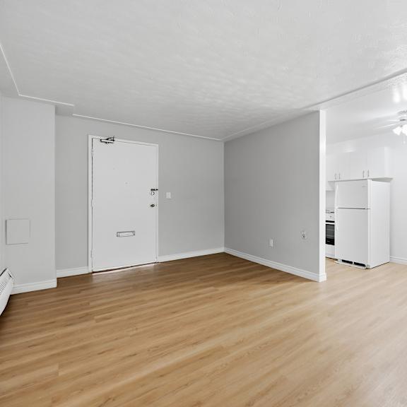a white room with wood flooring and a refrigerator.