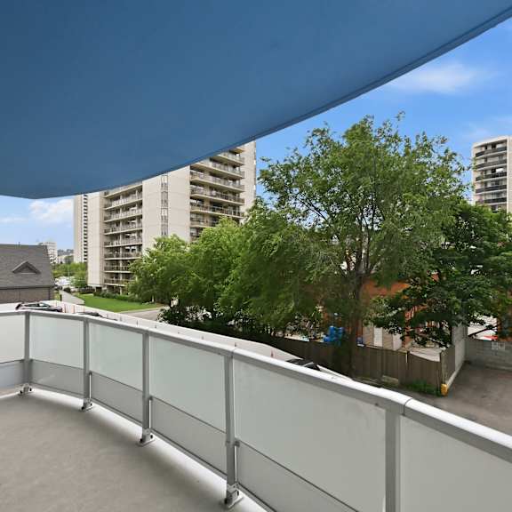 a balcony with a glass railing overlooks a parking lot and buildings.