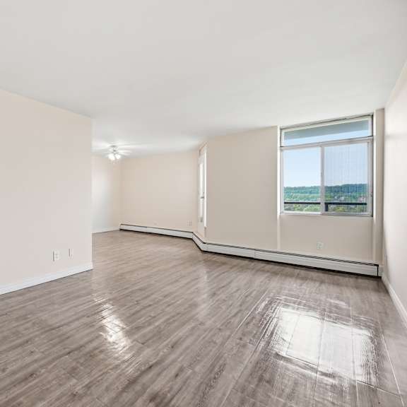 a spacious room with wooden flooring and a kitchen area in the background.