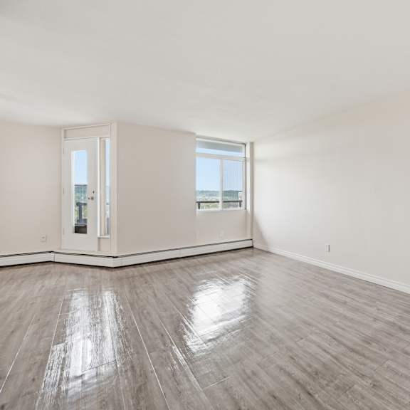a spacious room with wooden flooring and a view of the outside through a large window.