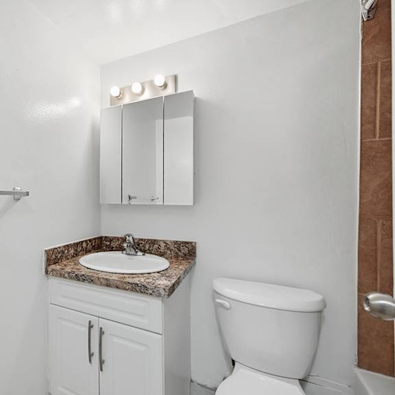 a white bathroom with a marble countertop and a toilet.