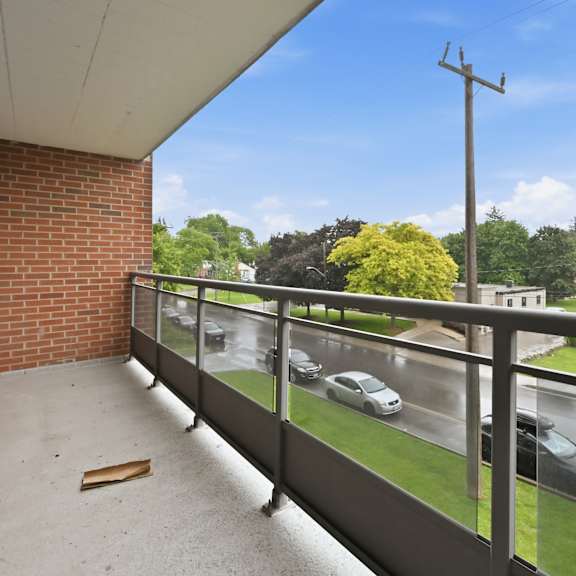 a balcony with a brick wall and a glass railing overlooking a street with cars.
