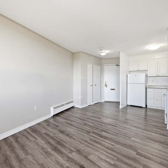 a spacious room with wood flooring and a kitchen area in the background.