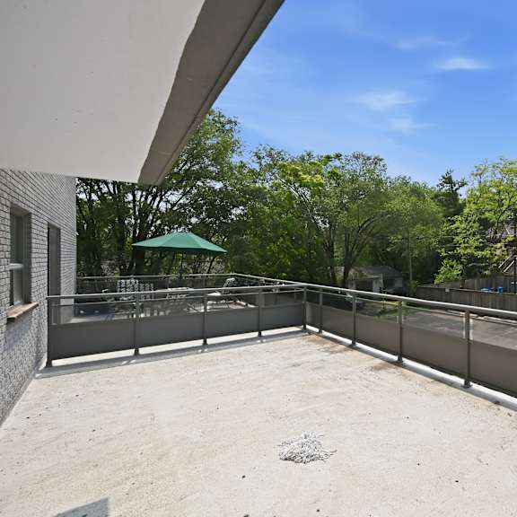 a rooftop patio with a metal railing and a car parked in the background.