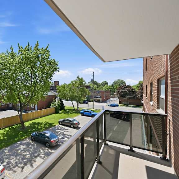a balcony overlooks a parking lot and a tree-lined street.