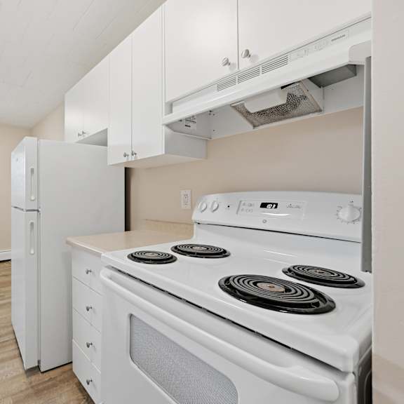 a white stove with four burners is in a kitchen with white cabinets.