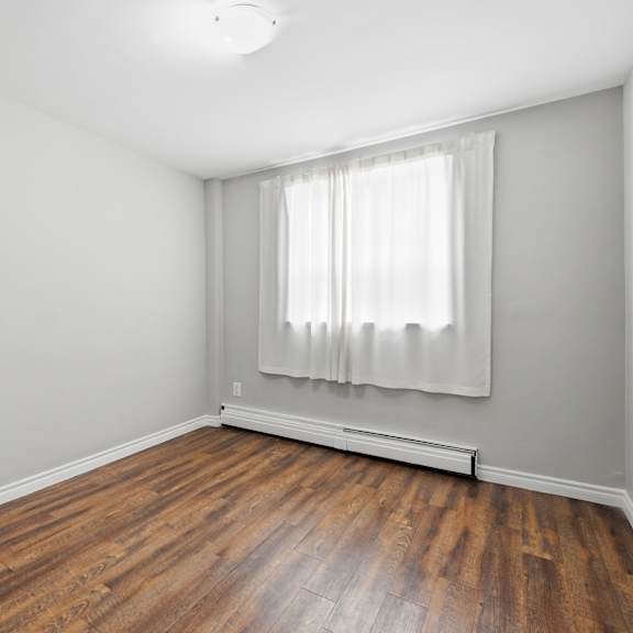a room with wooden floors and a window with white curtains.