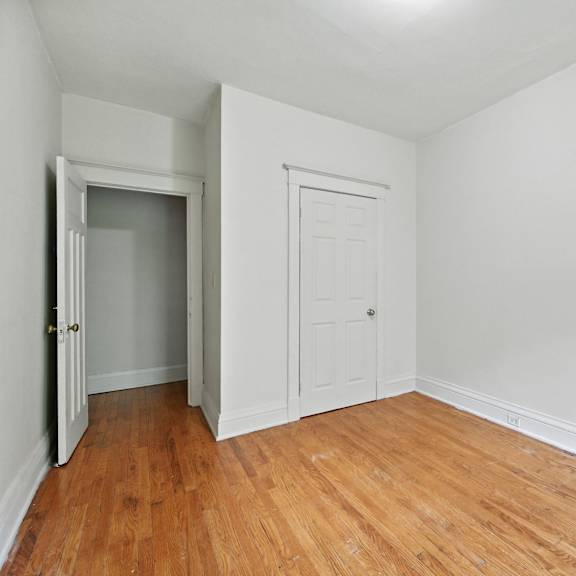 a room with a wooden floor and white walls, with a door and a wardrobe.