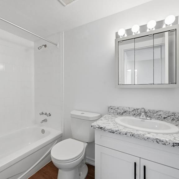 a white bathroom with a marble counter top and a round mirror.