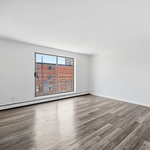 a room with wooden flooring and a window showing a brick building outside.