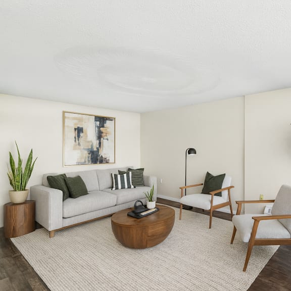 a living room with a grey couch, a wooden coffee table, a chair, a potted plant, and a painting on the wall.