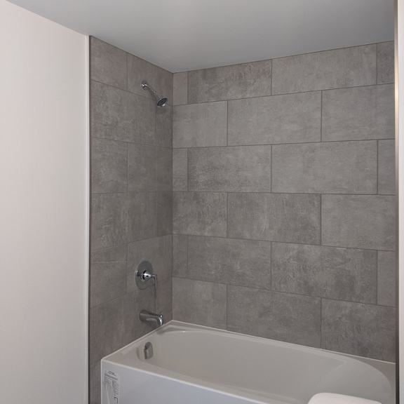 a white bathtub with a grey tile wall behind it.