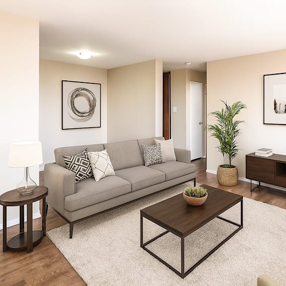 a living room with a grey couch, a coffee table, a side table, a chair, a potted plant, and pictures on the wall.