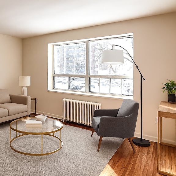 a living room with a beige couch, a grey armchair, a glass coffee table, and a framed artwork on the wall.