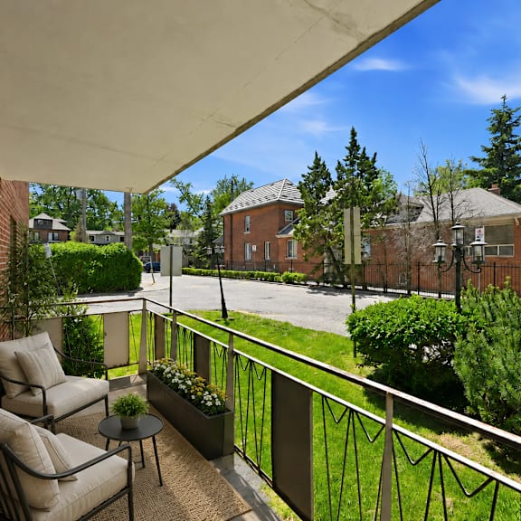 a balcony with a table and two chairs overlooks a green yard.