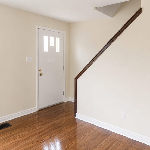a white door is in a room with wooden floors and a staircase.