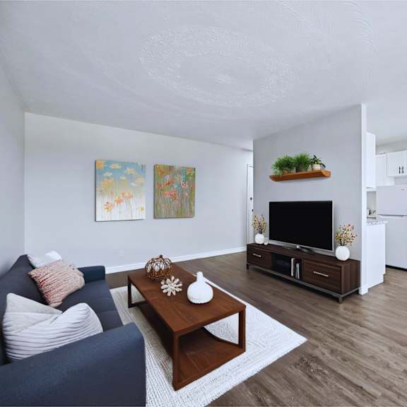 a living room with a blue couch, a coffee table, a tv, a dining table with chairs, and a painting on the wall.