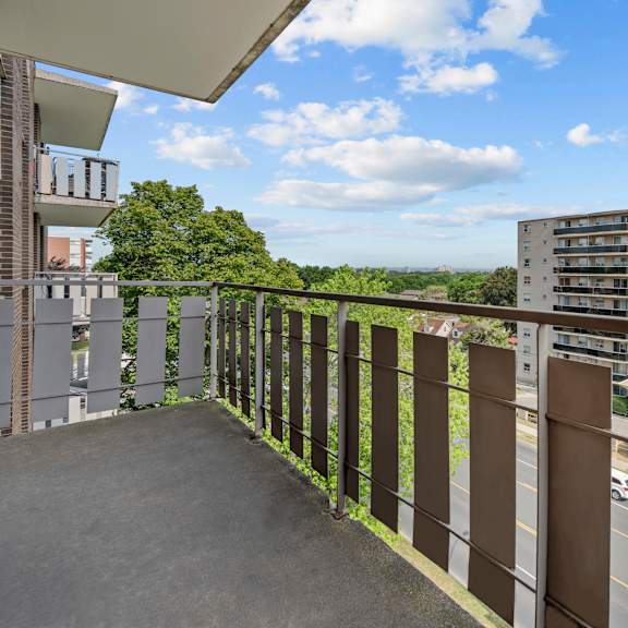 a balcony with a metal railing overlooks a road and buildings.