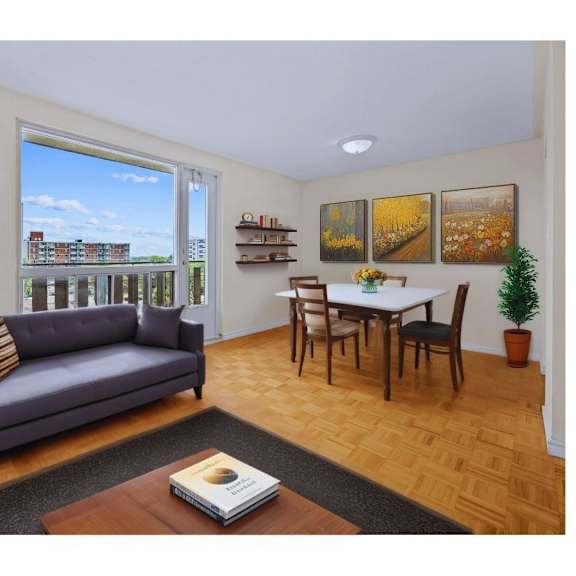 a living room with a grey couch, a small table with a lamp, a dining table with chairs, and pictures on the wall.