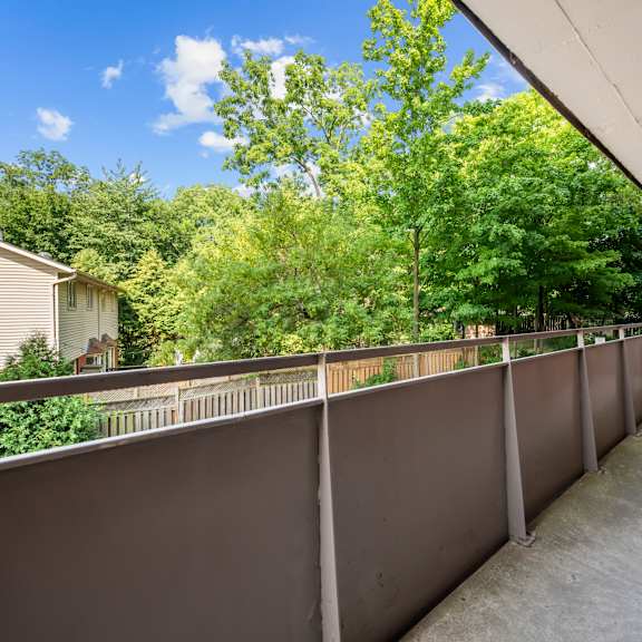 a long concrete balcony with a grey railing and trees in the background.