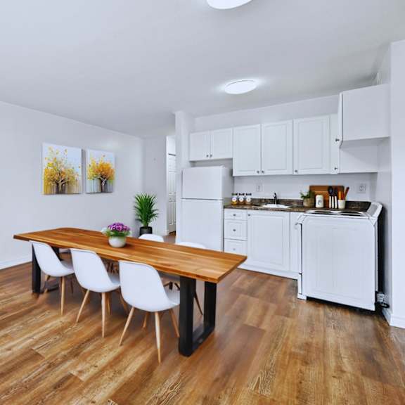 a kitchen with a table and chairs in the foreground and a refrigerator and cabinets in the background.