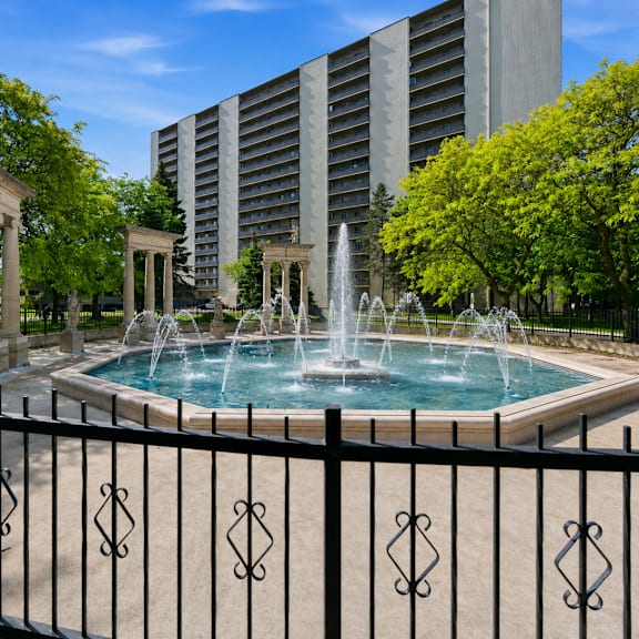 a fountain in the middle of a pool surrounded by a black fence.