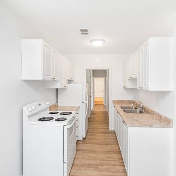 a white kitchen with a stove, sink, and cabinets.