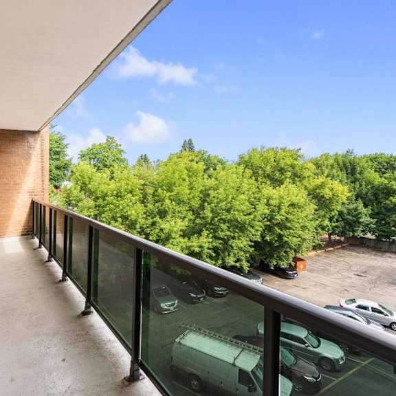a balcony with a brick wall and a glass railing overlooking a parking lot.