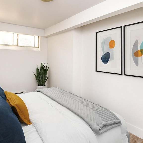 a bedroom with a bed, pillows, a plant, and two framed artworks on the wall.