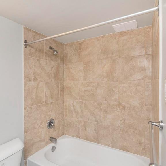 a bathroom with a white tub and beige tiled walls.