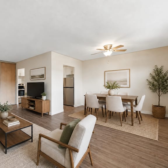 a living room with a grey couch, a coffee table, a chair, a potted plant, and a dining table set up.