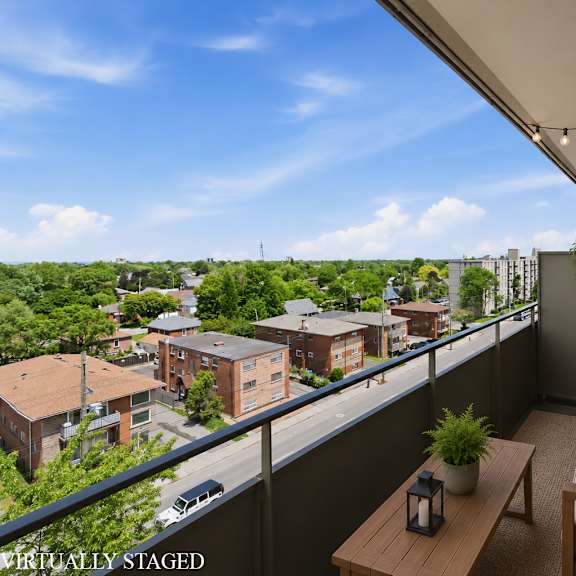 a balcony with a couch, table, and potted plants overlooks a residential area.
