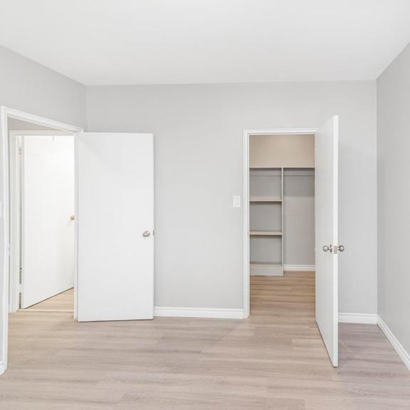 a white door is open to a room with a white wall and a white closet with shelves.
